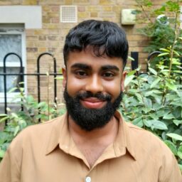 A photo of Look Ahead staff member Jaid Hussain, smiling while wearing a smart light brown-coloured shirt.