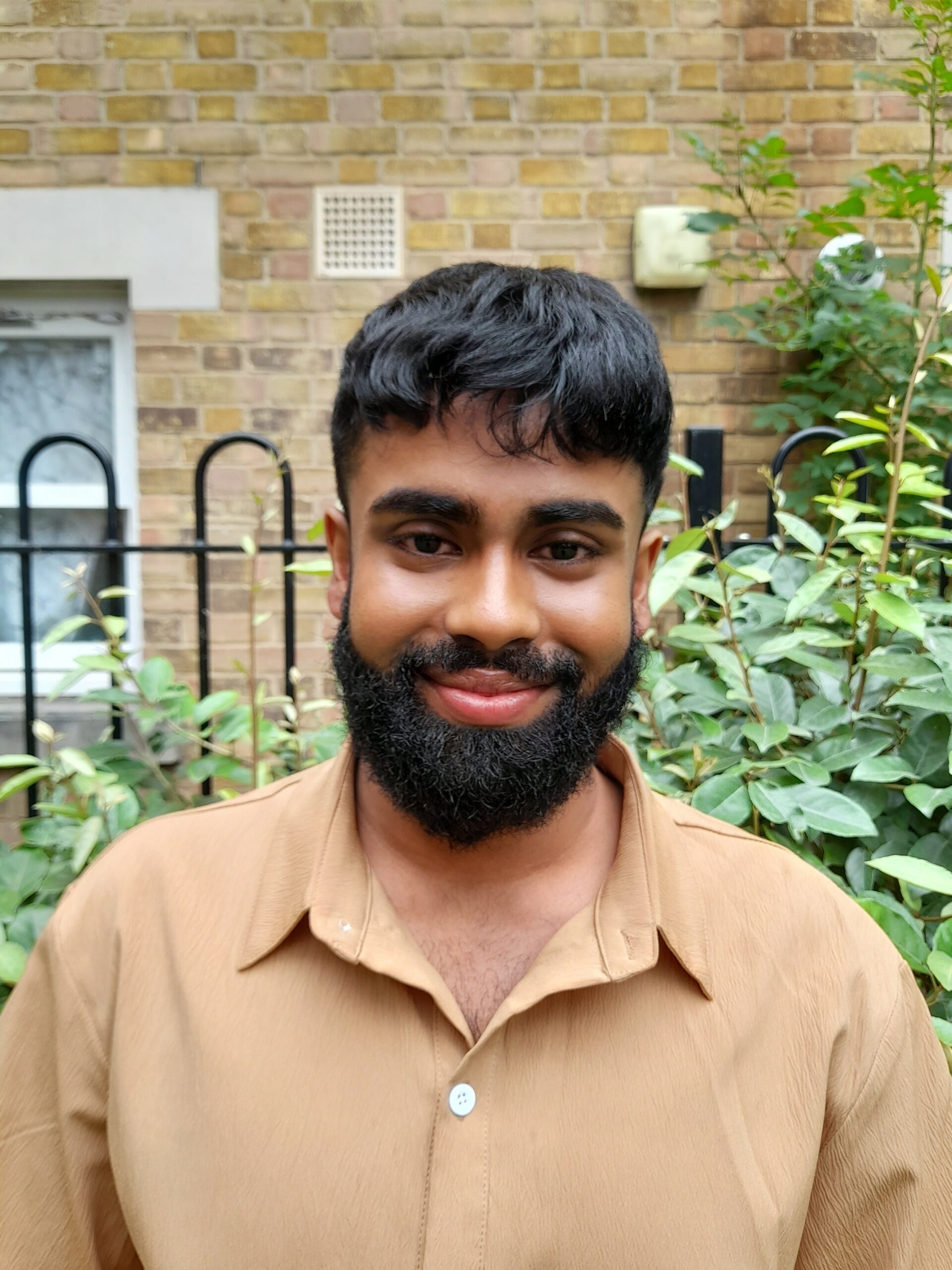 A photo of Look Ahead staff member Jaid Hussain, smiling while wearing a smart light brown-coloured shirt.